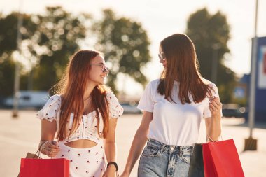 Günlük giysiler içinde iki güzel kadın ellerinde alışveriş çantaları, açık havada..