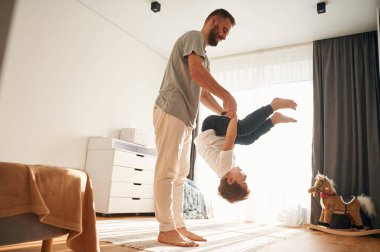 Çocuğu baş aşağı tutmak. Adam evcil odasında oğluyla oynuyor..