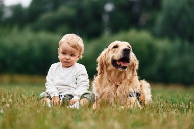 Yerde oturuyordum. Sahada Golden Retriever köpeği olan küçük çocuk.