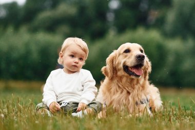 Yerde oturuyordum. Sahada Golden Retriever köpeği olan küçük çocuk.