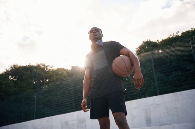 Kendine güvenen biri. Genç siyah adam basketbol topuyla dışarıda..