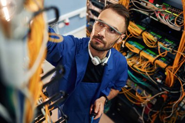 Kabloların idaresi. Genç adam sunucu odasında internet ekipmanı ve kablolarıyla çalışıyor..