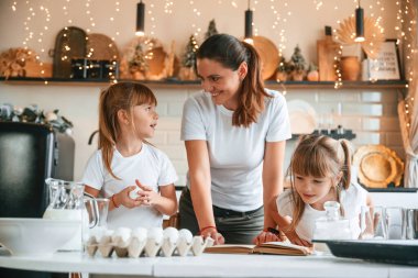 Mutfakta, çelenklerle birlikte. Anne ve iki küçük kızı yemek hazırlıyorlar..