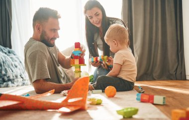 İki ebeveyn yerde oğluyla oynuyorlar. Bir sürü oyuncak..