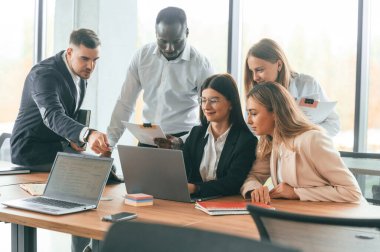 Masadaki kablosuz cihaz, dizüstü bilgisayar. Bir grup ofis çalışanı içeride birlikte..