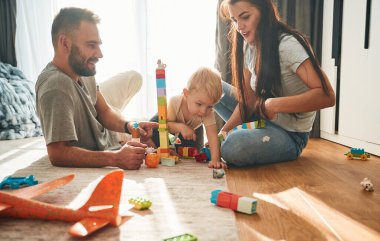 İki ebeveyn yerde oğluyla oynuyorlar. Bir sürü oyuncak..