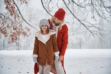 Ön manzara, ayakta. Anne ve kızı kış çayırlarında ve ormandalar..