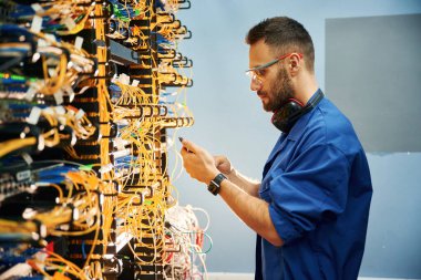 Yan görüş. Genç adam sunucu odasında internet ekipmanı ve kablolarıyla çalışıyor..