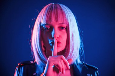 Parmaklar dudaktan, sessizlik. Beyaz saçlı kadın stüdyoda neon renkli..