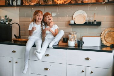 Halkın refahı. Mutlu iki küçük kız mutfaktaki masada otururken süt içiyor..