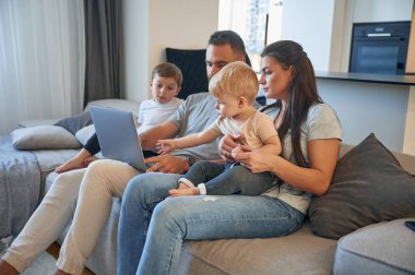 Bacaklarında dizüstü bilgisayarla. İki küçük çocuklu ebeveynler evcil odada birlikteler..