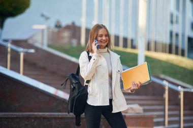Telefonla konuşuyorum. Gündelik giysiler içinde genç bir kız öğrenci dışarıda..