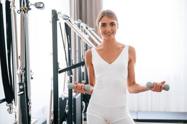 Ayakta ve gülümsüyor. Spor salonundaki genç kadın egzersiz yapıyor..