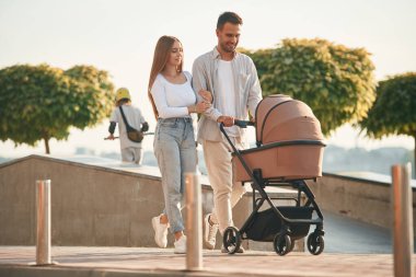 Arkadaki küçük yeşil ağaçlar. Bebek arabalı genç bir çift birlikte yürüyor..