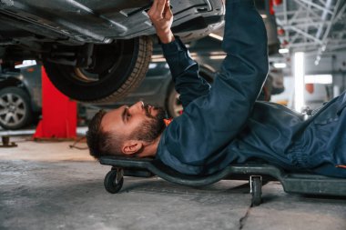 Yere uzanıyordu. Araba tamircisi otomobille garajda..