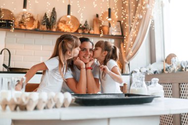 Aile günü. Anne ve iki küçük kızı mutfakta çelenklerle birlikte yemek hazırlıyorlar..