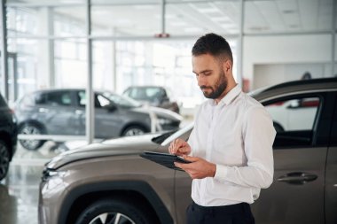 Siyah renkli tablet ellerinde. Resmi giyinen işçi oto kuaföründe..