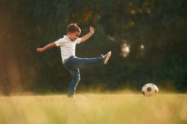 Yan görünüş, futbol oynamak. Küçük çocuk gündüz vakti dışarıda oynuyor..