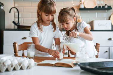 Sütü döküyorum. İki küçük kız mutfakta çelenklerle yemek hazırlıyor..