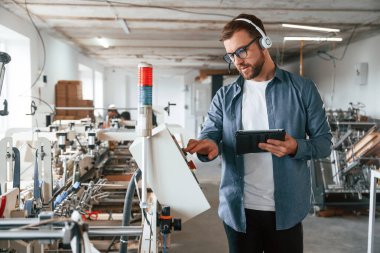 Kulaklıkla, tabletle. Yakışıklı adam ekolojik kutular üreten fabrikada çalışıyor..