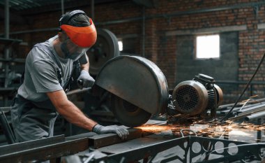 Metali kesme işlemi. Gri üniformalı genç fabrika işçisi.