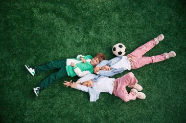 Üst Manzara. Uzanmak. Çocuklar yeşil futbol sahasında birlikte eğleniyorlar..