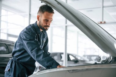 Yan görüş, kaput açık. Araba tamircisi otomobille garajda..