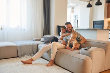 Gülümseyen, pozitif yüz ifadesi. İki erkek çocuğu olan baba kanepede oturuyor..