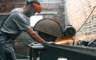 İşine odaklan, metali kes. Fabrikadaki gri üniformalı genç adam..