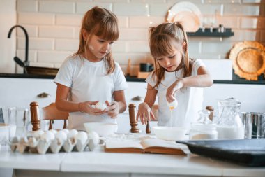 Un ve yumurtalar masaya. İki küçük kız mutfakta çelenklerle yemek hazırlıyor..