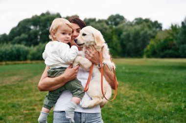 Güzel bir kadın sahada duruyor ve kucağında köpek yavrusu ve küçük bir çocuk var..