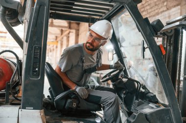 Profesyonel forklift sürücüsü. Gri üniformalı genç fabrika işçisi.