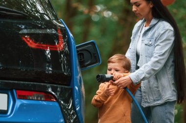 İşlemi öğreniyorum. Anne ve küçük oğlu dışarıda elektrikli arabayı şarj ediyorlar..