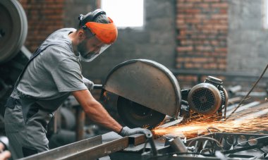 Yan görünüş, metali kesmek. Gri üniformalı genç fabrika işçisi.