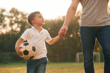 Yürüyen ve futbol topu tutan. Baba ve küçük oğlu dışarıda oynuyor ve eğleniyorlar..