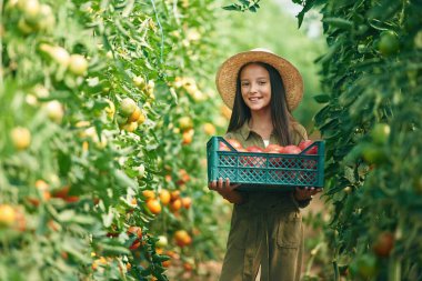 Hasır şapkalı ve sebzeli. Küçük kız domateslerle bahçede..