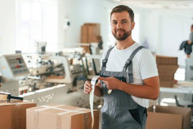 Poz veren, neşeli erkek. Yakışıklı adam ekolojik kutular üreten fabrikada çalışıyor..