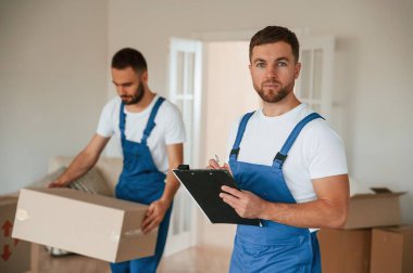 Evraklar ellerinde. Bir odada hareket eden iki servis çalışanı.