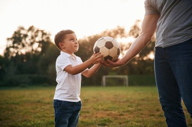 Çocuk futbol topunu alıyor. Baba ve küçük oğlu dışarıda oynuyor ve eğleniyorlar..