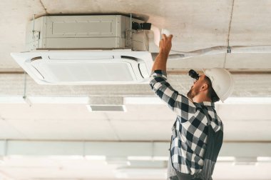 Havalandırma sistemi tavanda, tamir ediliyor. Üniformalı tamirci tamamlanmamış binada..