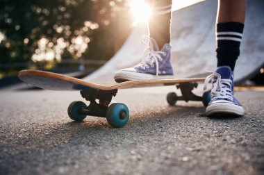 Tek ayak üzerinde kaykay yapmak. Mavi ayakkabılı genç bir kızın bacakları..