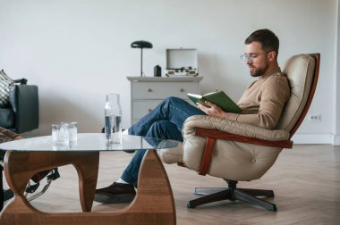 Erkek psikolog ofisinde not defteriyle sandalyede oturuyor..