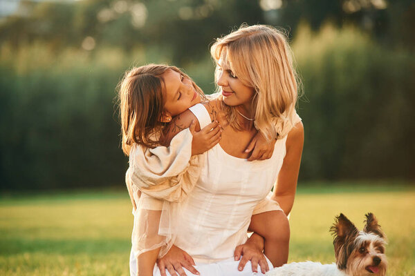 Conception of love and care. Mother with her daughter and cute dog are on the field outdoors.