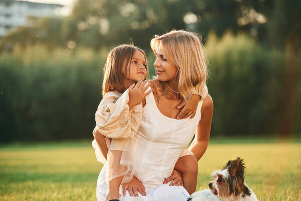 Conception of love and care. Mother with her daughter and cute dog are on the field outdoors.