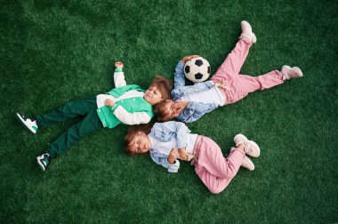 Üst Manzara. Uzanmak. Çocuklar yeşil futbol sahasında birlikte eğleniyorlar..