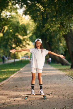 Halk parkında duruyor. Dışarıda kaykaylı mutlu küçük kız.