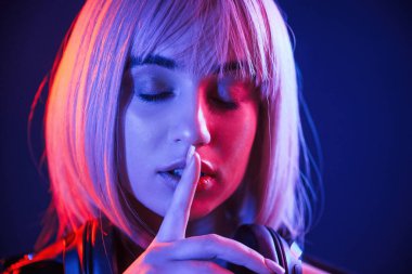 Parmaklar dudaktan, sessizlik. Beyaz saçlı kadın stüdyoda neon renkli..