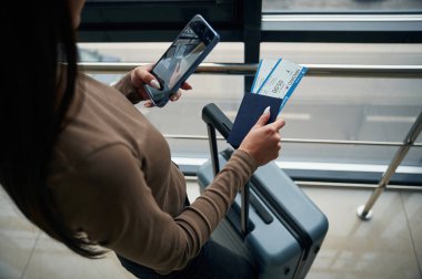 Akıllı telefonu tutuyorsun. Havaalanı koridorunda biletlerle gezen kadın yolcuların yakın görüntüsü..