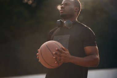 Açık havada güneş ışığı. Genç siyah adam basketbol topunun yanında..