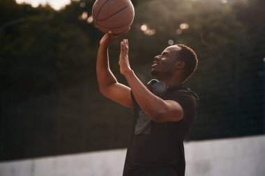 Açık havada güneş ışığı. Genç siyah adam basketbol topunun yanında..